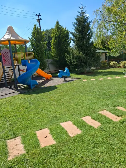 Şehitkamil villa bahçesinde çocuk oyun alanı, çime döşeli basamak taşları ve ibreli ağaç perdesi